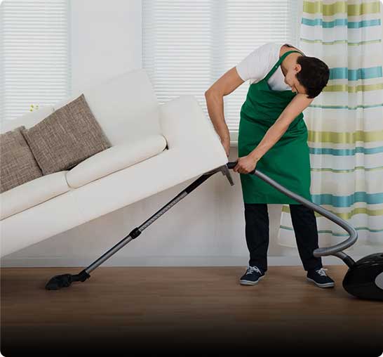 Man using a vacuum cleaner to clean underneath a couch.